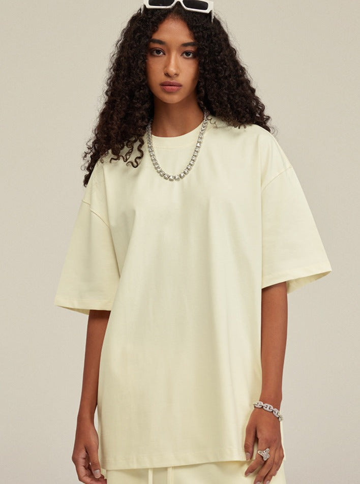 Frau in cremefarbenem Oversize-T-Shirt, modisch mit Kette und lockigem Haar. Trendige Damenmode, lässiger Look, Streetwear-Stil.