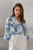 Elegante Damenbluse mit blau-weißem Toile-de-Jouy-Muster, kombiniert mit stilvoller weißer Hose. Perfekt für modische, zeitlose Outfits.