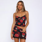 Frau in einem schwarzen, geblümten Kleid mit roten Rosen, Spaghettiträgern und figurbetontem Schnitt. Perfekt für Sommermode und Partykleidung.