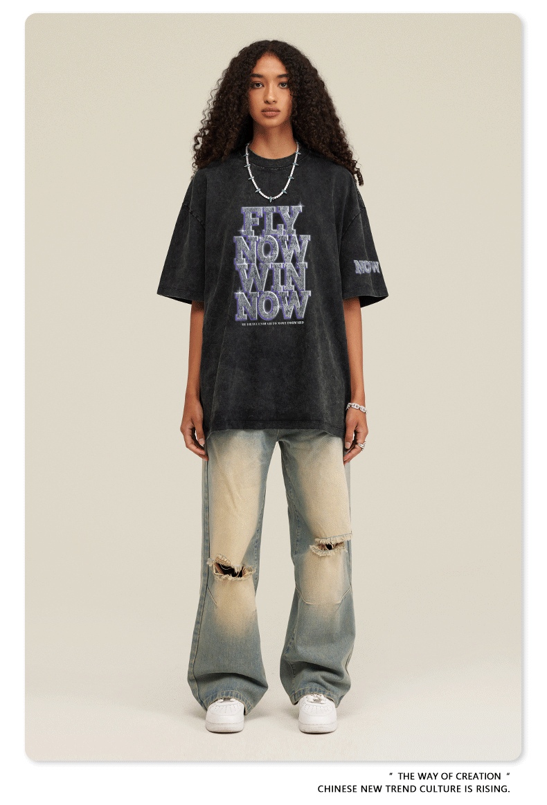 Schwarzes T-Shirt mit "Fly Now Win Now"-Aufdruck, getragen von einer Person mit lockigem Haar. Modetrend, urbaner Stil, lässige Kleidung.