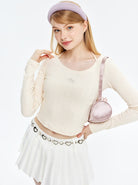 Junge Frau in modischem Outfit: cremefarbener Pullover, weißer Faltenrock, rosa Stirnband und Tasche. Trendige Damenmode, stilvoll und elegant.