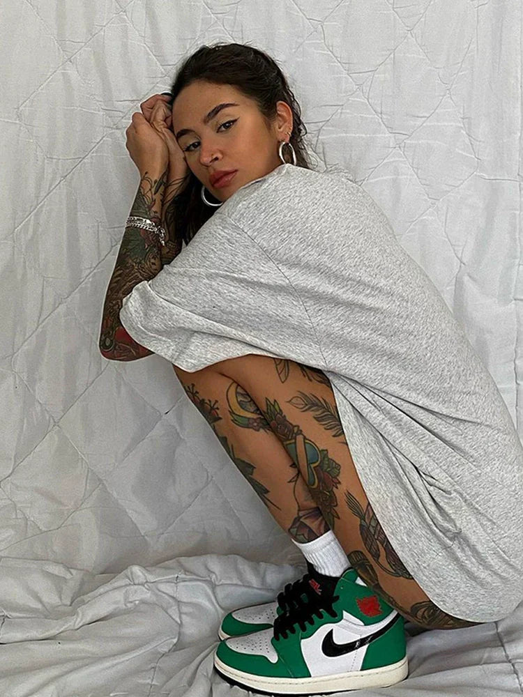Frau in grauem T-Shirt und tätowierten Beinen trägt grün-weiße Nike-Sneaker. Streetwear, Mode, Tattoos, Nike, Sneaker-Trend.