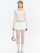Damenmode: Elegantes Outfit mit cremefarbenem Langarmshirt, weißem Faltenrock, gepunkteten Strumpfhosen und rosa Handtasche. Ideal für Frühling.