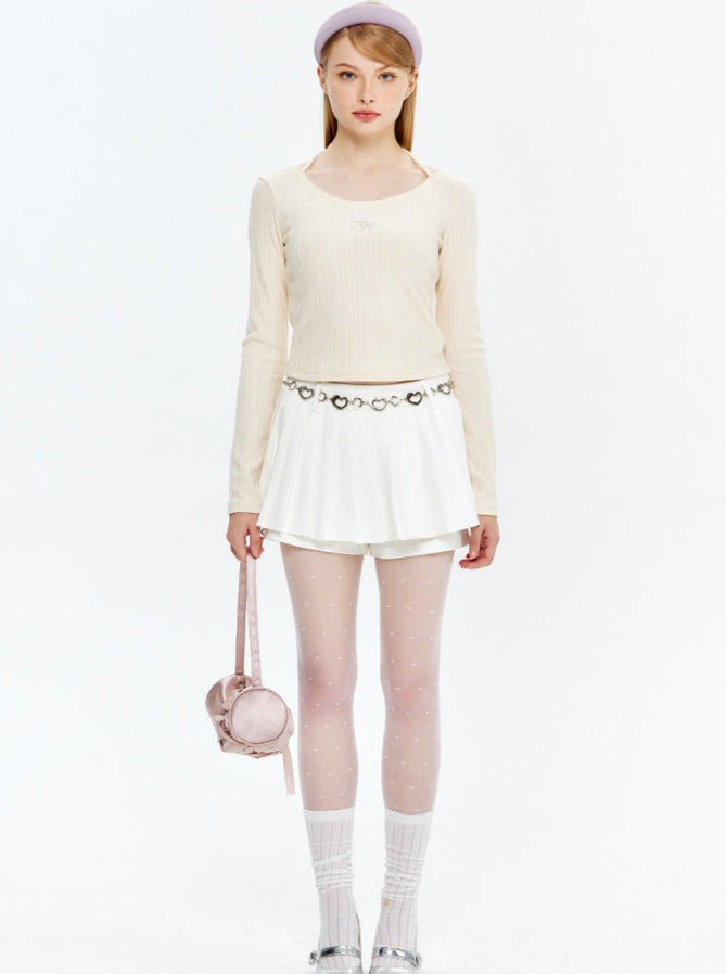 Damenmode: Elegantes Outfit mit cremefarbenem Langarmshirt, weißem Faltenrock, gepunkteten Strumpfhosen und rosa Handtasche. Ideal für Frühling.