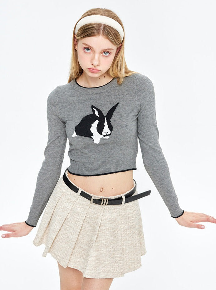 Grauer Pullover mit Hasenmotiv, kombiniert mit beigem Faltenrock. Modetrend, Damenmode, stilvoller Look, Herbstkollektion, Streetwear.