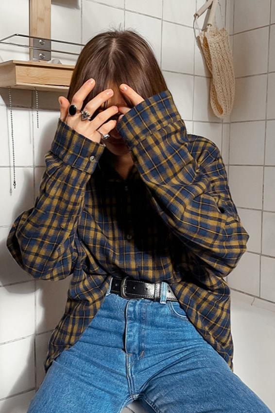 Frau in kariertem Hemd und blauer Jeans sitzt in einem gefliesten Raum. Modetrend, lässiger Stil, Herbstmode, Damenbekleidung.