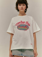 Junge Frau trägt weißes T-Shirt mit "Overdue flair"-Aufdruck, kombiniert mit Jeansrock. Modetrend, lässiger Stil, Streetwear, Damenmode.