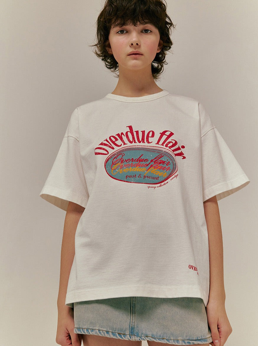 Junge Frau trägt weißes T-Shirt mit "Overdue flair"-Aufdruck, kombiniert mit Jeansrock. Modetrend, lässiger Stil, Streetwear, Damenmode.
