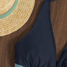 Strohhut und schwarzer Badeanzug auf Holzhintergrund. Sommermode, Strandaccessoires, stilvoller Look für Urlaub und Freizeit.