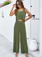Frau in grünem Sommer-Zweiteiler vor weißer Wand, modisch mit Sonnenbrille. Perfekt für stilvolle Sommermode und Freizeitoutfits.
