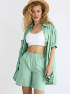 Frau in mintgrünem Sommeroutfit mit Hemd und Shorts, weißem Top und Strohhut. Modetrends, Damenbekleidung, Sommermode, lässiger Stil.