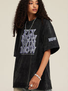 Schwarzes Oversize-T-Shirt mit "FLY NOW WIN NOW"-Aufdruck, lässiger Streetwear-Stil, ideal für trendige Mode und urbanen Look.