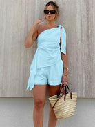 Frau in hellblauem, schulterfreiem Jumpsuit mit Sonnenbrille und Strohtasche. Sommermode, eleganter Look, trendige Damenbekleidung.