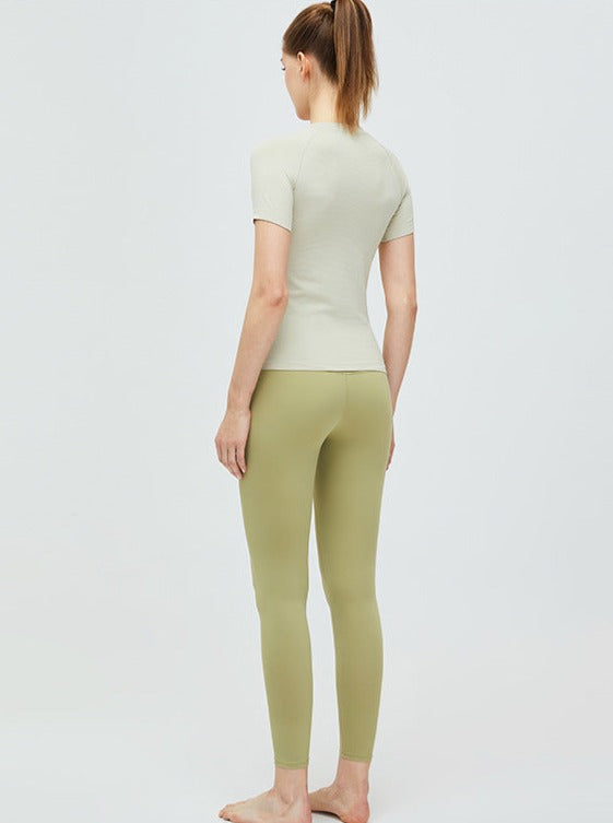 Frau in beiger Sportbekleidung, bestehend aus T-Shirt und Leggings. Ideal für Yoga und Fitness. Bequeme, atmungsaktive Materialien.