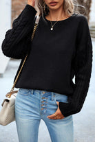 Damenmode: Schwarzer Strickpullover mit Zopfmuster-Ärmeln, kombiniert mit blauen Jeans und einer eleganten Umhängetasche. Perfekt für den Herbst.