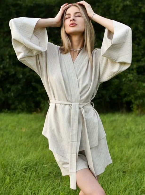 Frau in beigem Kimono-Kleid posiert im Freien. Modetrend, lässiger Stil, Sommermode, Damenbekleidung, elegantes Design, Naturhintergrund.