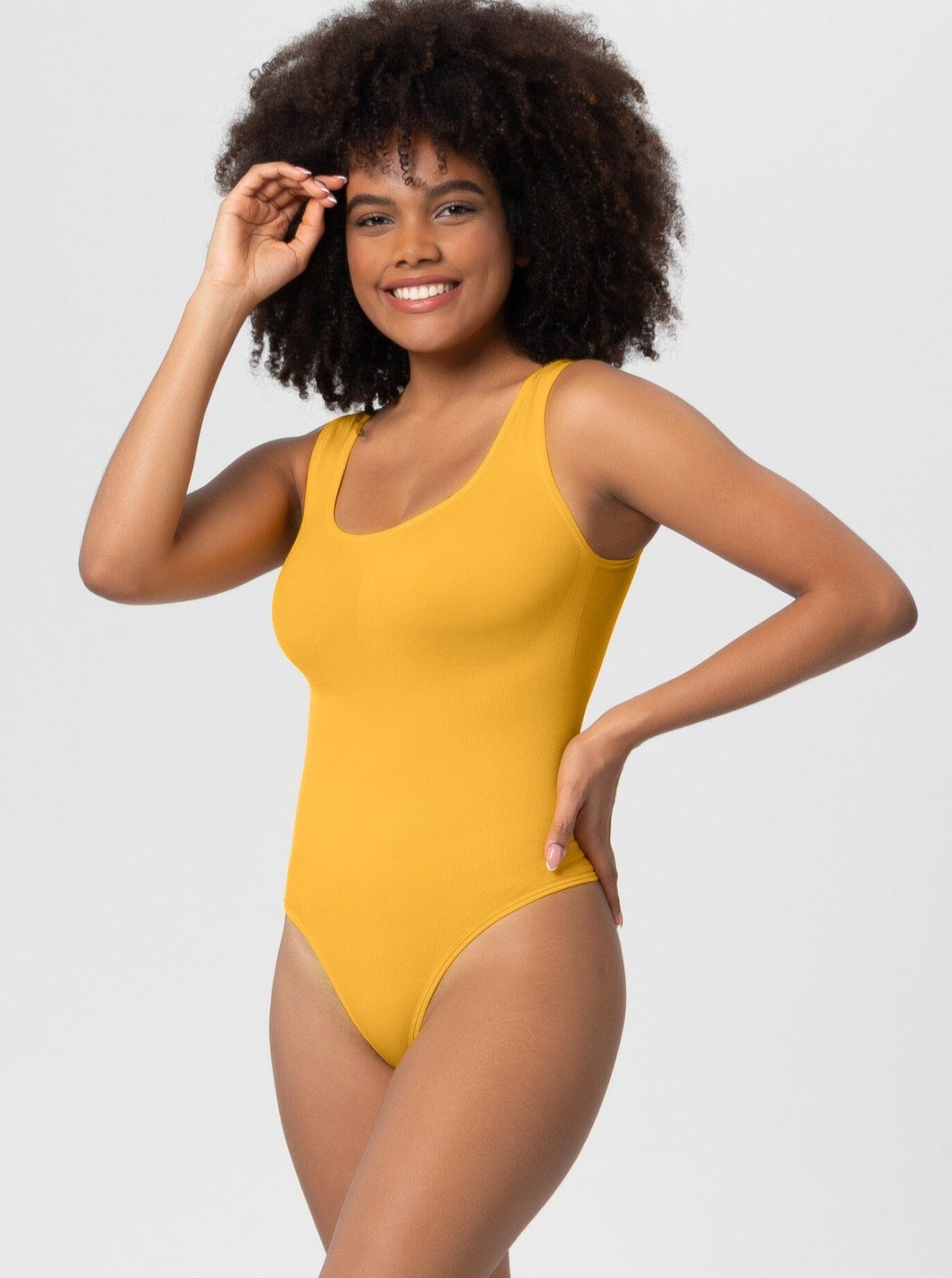 Frau in gelbem Body, lächelnd, vor weißem Hintergrund. Modetrend, Damenmode, Sommeroutfit, bequeme Kleidung, stilvoller Einteiler.