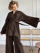 Frau in elegantem, schwarzem Kimono-Set mit weitem Schnitt, stehend vor modernen Stühlen. Modetrend, Damenbekleidung, stilvoll, bequem.