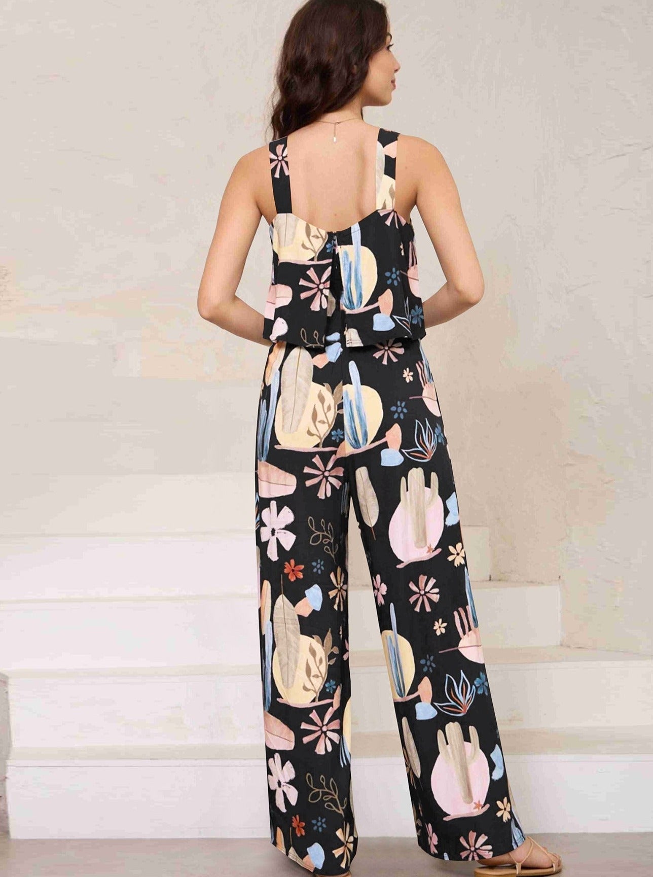 Frau in schwarzem Jumpsuit mit buntem Kaktus- und Blumenmuster, ärmellos, modisch, lässig, ideal für Sommermode und Freizeitkleidung.