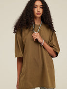 Frau in olivgrünem Oversize-T-Shirt, lockiges Haar, trägt Halskette und Armband. Modetrend, lässiger Stil, Streetwear, Damenmode.
