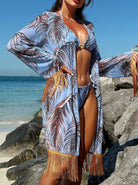 Frau im blauen Strandkimono mit Palmenmuster und Fransen, Bikini, am Felsenstrand. Sommermode, Strandbekleidung, tropischer Stil.