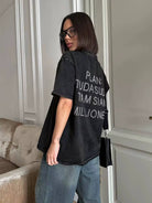Frau in schwarzem T-Shirt mit Aufschrift, lässiger Stil, Jeans, moderne Brille, modisches Outfit, urbaner Look, trendige Damenmode.