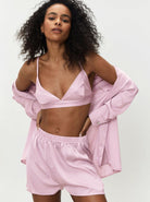 Frau in rosa Satin-Pyjama-Set mit Hemd, Shorts und Bralette. Modetrend, Nachtwäsche, bequeme Damenbekleidung, stilvoller Look.