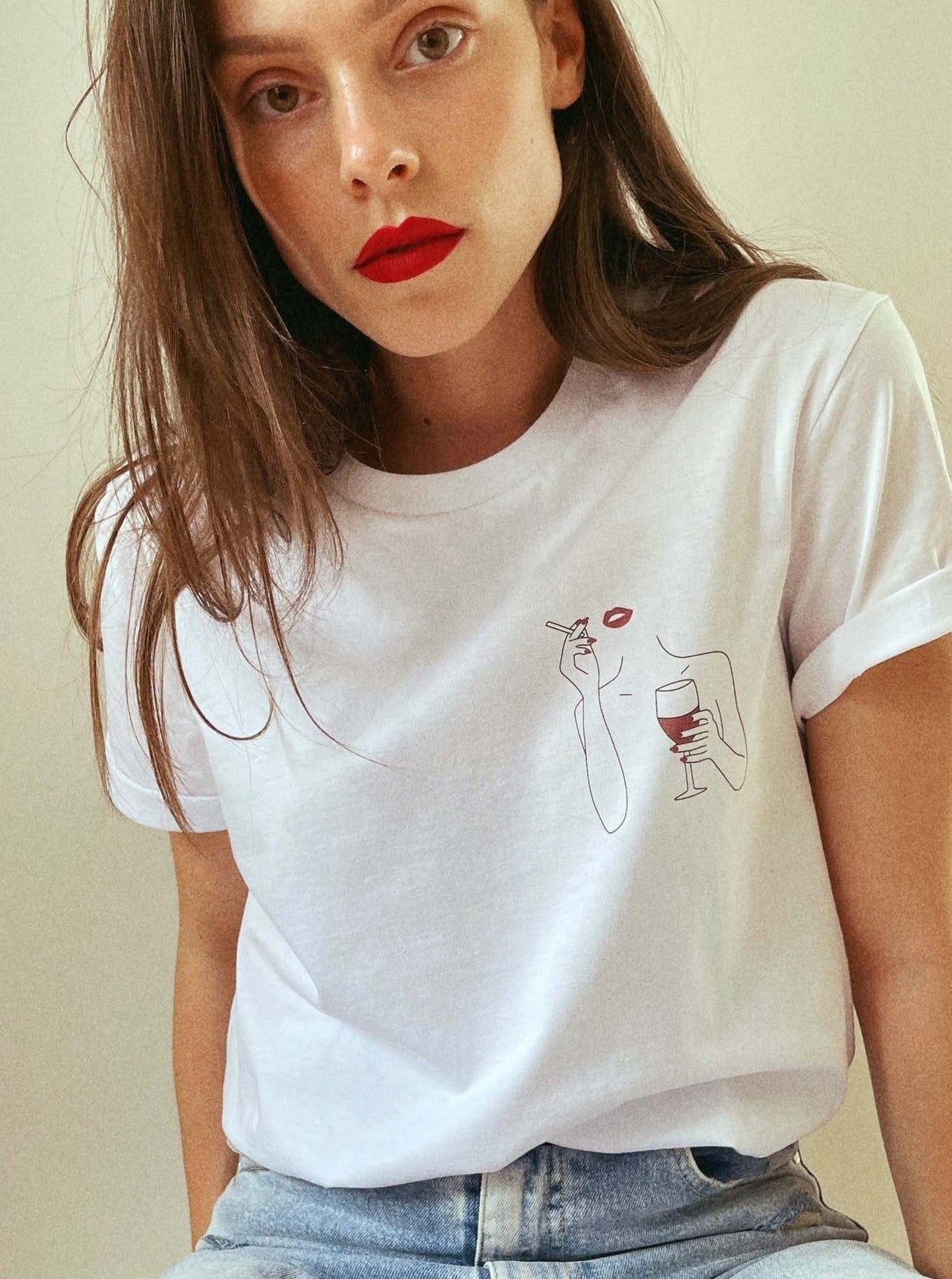 Frau in weißem T-Shirt mit minimalistischer Grafik, rotem Lippenstift und Weinglas. Modetrend, lässiger Stil, Damenmode, Streetwear.