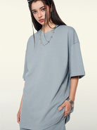 Frau in grauem Oversize-T-Shirt, lässiger Streetwear-Look, modisches Outfit, urbaner Stil, trendige Damenmode, minimalistisches Design.