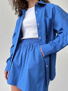 Frau in blauer Bluse und Rock, kombiniert mit weißem T-Shirt. Modetrend, Damenbekleidung, lässiger Stil, Sommeroutfit, elegantes Design.