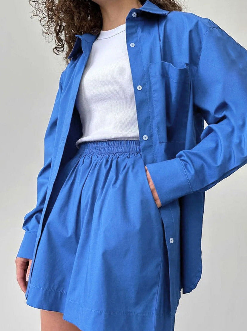 Frau in blauer Bluse und Rock, kombiniert mit weißem T-Shirt. Modetrend, Damenbekleidung, lässiger Stil, Sommeroutfit, elegantes Design.
