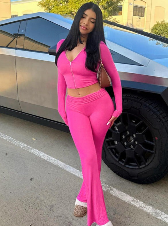 Frau in pinkem Trainingsanzug posiert vor einem futuristischen Auto. Modetrend, Streetstyle, sportliche Kleidung, urbaner Look, stilvoll.