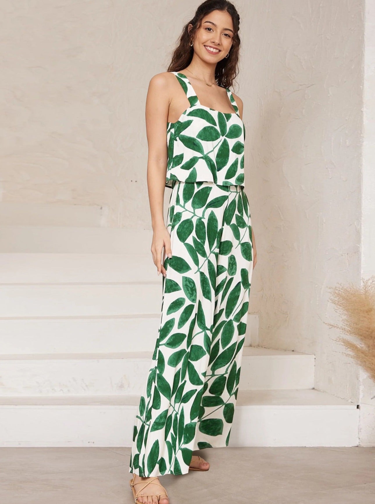 Frau in stilvollem, ärmellosem Jumpsuit mit grünem Blattmuster, ideal für Sommermode. Perfekt für lässige Anlässe und trendige Outfits.