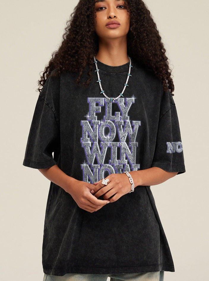 Schwarzes Oversize-T-Shirt mit "FLY NOW WIN NOW"-Aufdruck, lässiger Streetwear-Stil, ideal für trendige Mode und urbanen Look.