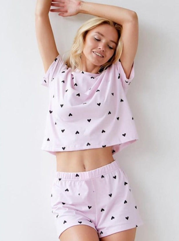 Frau in rosa Pyjama-Set mit Herzmuster, lächelnd und entspannt. Bequeme Nachtwäsche, modisch, ideal für Damen, Schlafanzug, Loungewear.