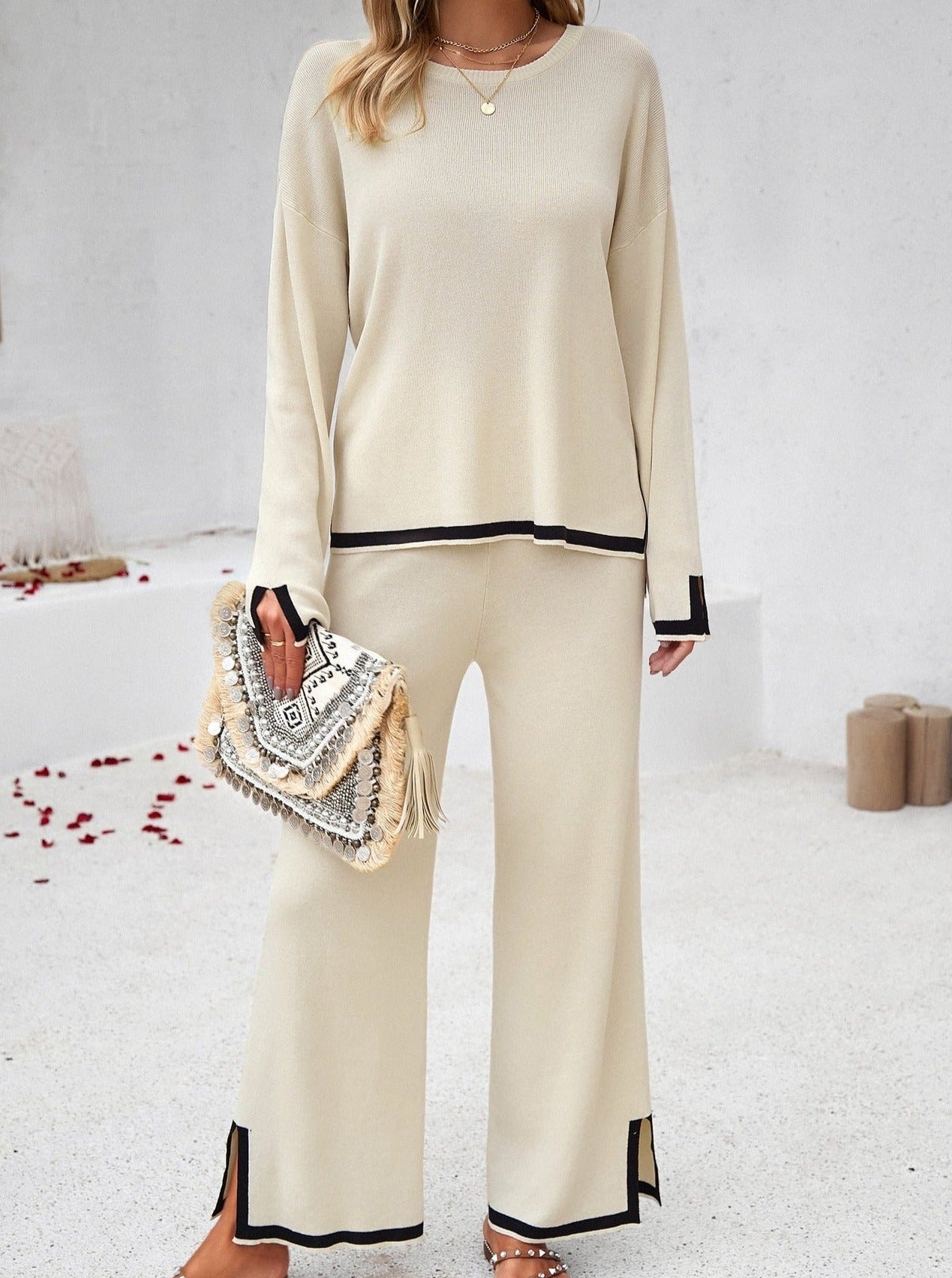 Damen-Outfit in Beige: Eleganter Zweiteiler mit Pullover und Hose, verziert mit schwarzem Saum. Perfekt für stilvolle Freizeit- und Bürolooks.