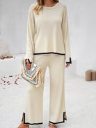 Damen-Outfit in Beige: Eleganter Zweiteiler mit Pullover und Hose, verziert mit schwarzem Saum. Perfekt für stilvolle Freizeit- und Bürolooks.
