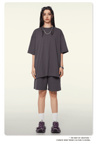 Dunkelgraues Oversize-T-Shirt und Shorts-Set, lässiger Streetwear-Look, ideal für trendige Mode, kombiniert mit lila Sneakers und Accessoires.