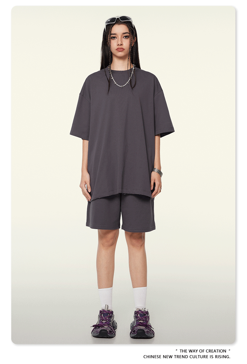 Dunkelgraues Oversize-T-Shirt und Shorts-Set, lässiger Streetwear-Look, ideal für trendige Mode, kombiniert mit lila Sneakers und Accessoires.