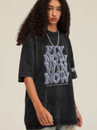 Schwarzes Oversize-T-Shirt mit "Fly Now Win Now"-Aufdruck, getragen von einer Person mit lockigem Haar. Trendige Streetwear-Mode für Jugendliche.