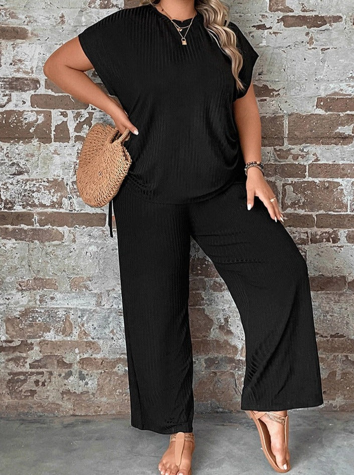 Damen-Outfit in Schwarz, bestehend aus lockerem T-Shirt und weiten Hosen, kombiniert mit Strohtasche. Perfekt für lässige Sommermode.