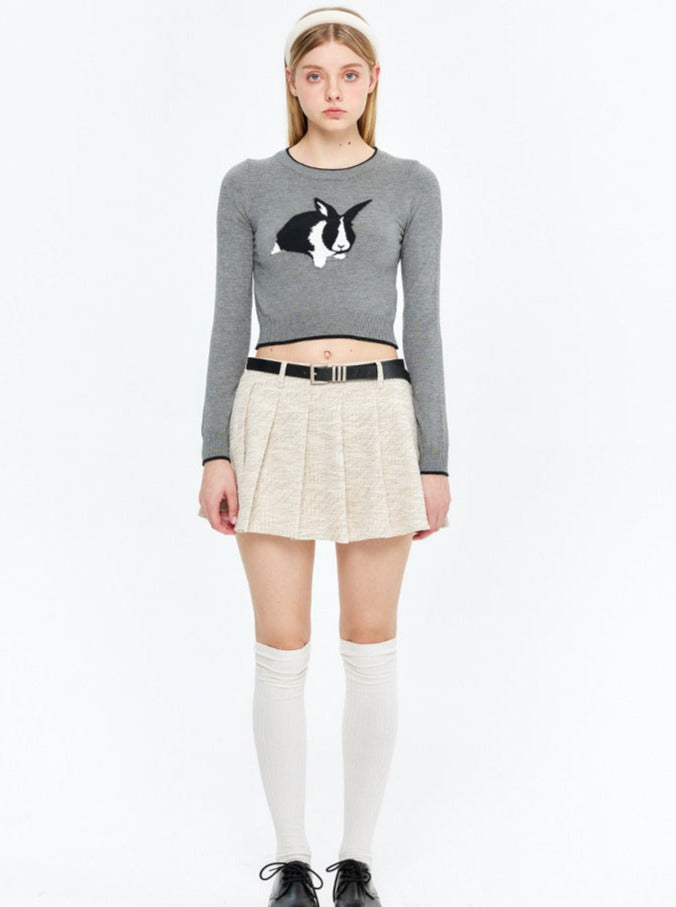 Graues Langarmshirt mit Hasenmotiv, kombiniert mit beigem Faltenrock und Kniestrümpfen. Modetrend, Damenbekleidung, Streetstyle.