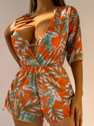 Frau in orangefarbenem, tropisch bedrucktem Jumpsuit mit tiefem Ausschnitt. Sommermode, Strandkleidung, tropisches Design, stilvoller Look.