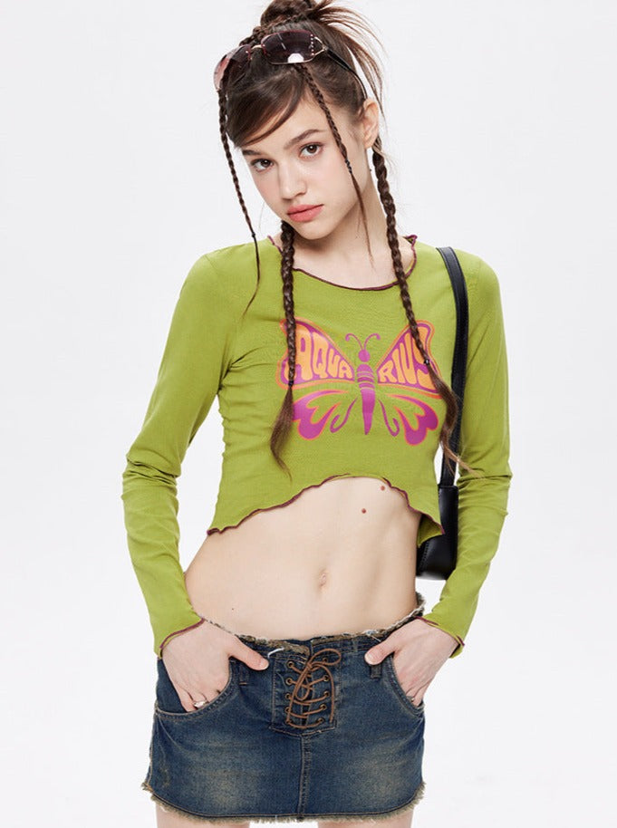 Junge Frau in grünem Langarmshirt mit Schmetterlingsmotiv und Jeansrock. Modetrend, Streetwear, lässiger Stil, jugendliche Mode.