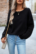 Frau in schwarzem Pullover und blauer Jeans, trägt goldene Halskette und Ohrringe, mit grauer Handtasche. Modetrends, Damenmode, Streetstyle.