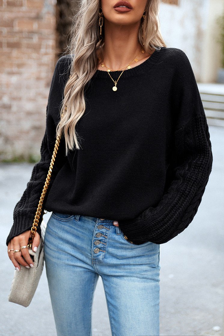 Frau in schwarzem Pullover und blauer Jeans, trägt goldene Halskette und Ohrringe, mit grauer Handtasche. Modetrends, Damenmode, Streetstyle.