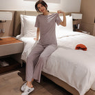 Frau in grauem Pyjama sitzt auf einem Bett in modernem Schlafzimmer. Bequeme Nachtwäsche, stilvolles Design, gemütliche Atmosphäre.