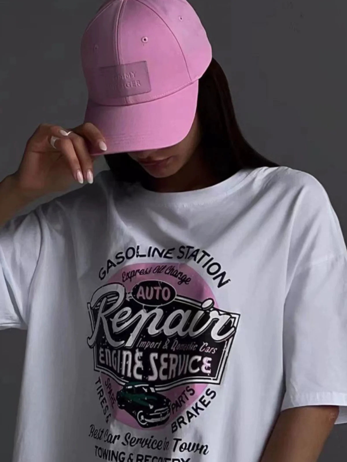 Frau mit rosa Baseballkappe und weißem T-Shirt mit "Auto Repair" Grafik. Modetrend, Streetwear, lässiger Stil, urbaner Look, Damenmode.