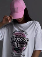 Frau mit rosa Baseballkappe und weißem T-Shirt mit "Auto Repair" Grafik. Modetrend, Streetwear, lässiger Stil, urbaner Look, Damenmode.