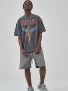 Junger Mann in grauem Nirvana-T-Shirt mit Engelsmotiv, grauen Shorts und Sneakers. Streetwear, lässiger Stil, Musik-Fanmode.